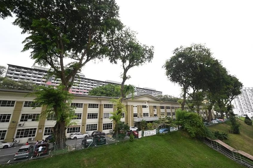 The former Upper Barracks today: a long colonial-era building on a grassy slope with mature trees, public housing blocks behind